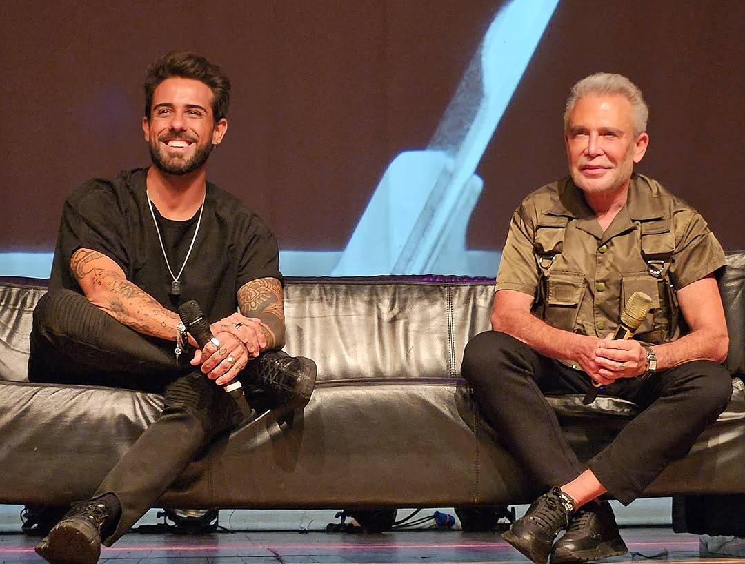Rapha Preto numa palestra, ao lado de um convidado, no palco